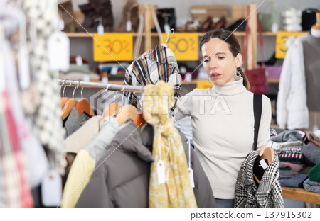 Woman chooses checkered jacket searches for fashionable clothes in clothing boutique Woman chooses checkered jacket searches for fashionable clothes in clothing boutique 137915302