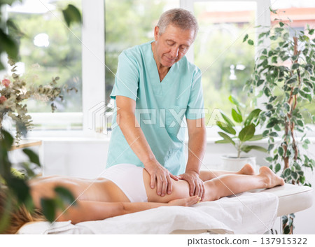 Skilled old masseur conducting hip massage for woman client 137915322