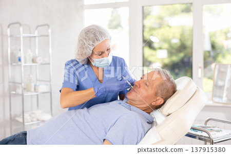 Woman cosmetologist makes injection in lips of man 137915380