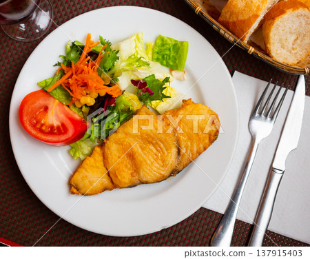 On plate there is small portion of salad of fresh vegetables and piece of fried fillet of white fish On plate there is small portion of salad of fresh vegetables and piece of fried fillet of white fish 137915403