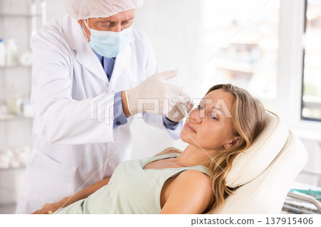 Male doctor gives injection and performs procedure of lip augmentation of female patient in clinic. Male doctor gives injection and performs procedure of lip augmentation of female patient in clinic. 137915406