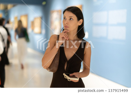Young woman in summer clothes looking at paintings in museum 137915499