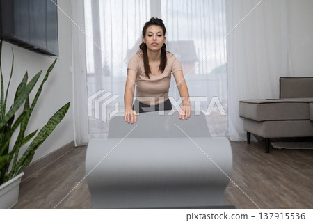 Woman Unrolling Yoga Mat in Her Living Room for an at Home Workout 137915536