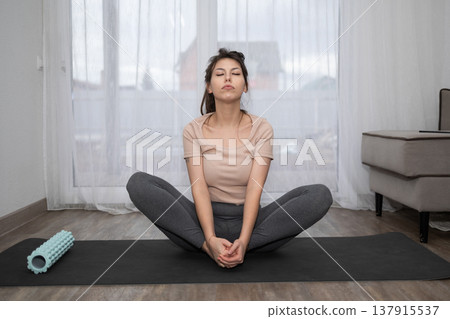 Woman Practices Yoga at Home During Afternoon With Foam Roller Nearby Woman Practices Yoga at Home During Afternoon With Foam Roller Nearby 137915537