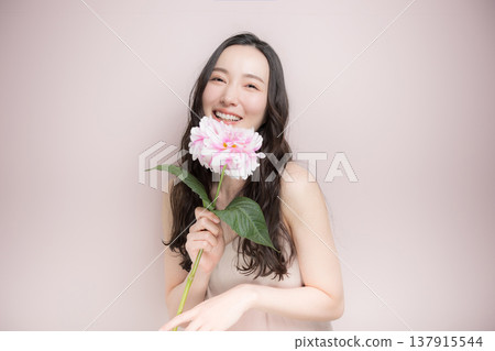 A woman with a dahlia flower, exuding a blissful pink spring image, looking directly at the camera in a beauty image. A woman with a dahlia flower, exuding a blissful pink spring image, looking directly at the camera in a beauty image. 137915544