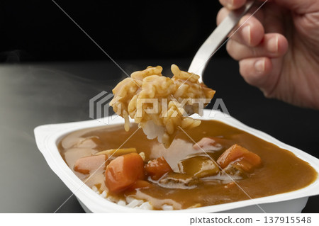 用湯匙舀起淋有速食咖哩的包裝米飯。 用湯匙舀起淋有速食咖哩的包裝米飯。 137915548