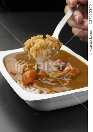 用湯匙舀起淋有速食咖哩的包裝米飯。 137915549