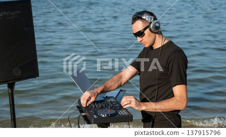 Caucasian man works as a DJ on the beach.  137915796