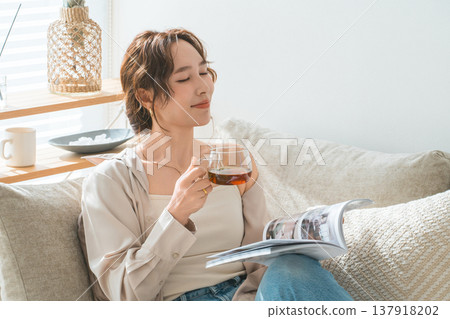 A stylish Asian woman sitting on the sofa in the living room and reading a magazine during tea time A stylish Asian woman sitting on the sofa in the living room and reading a magazine during tea time 137918202