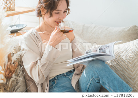 A stylish Asian woman sitting on the sofa in the living room and reading a magazine during tea time 137918203