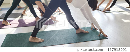 Close-up of yoga class stretching in triangle pose on mats under soft daylight Close-up of yoga class stretching in triangle pose on mats under soft daylight 137918991