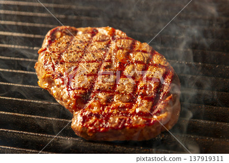 Raw steak before grilling; smoke rising from the hot grill; a realistic scene of teppanyaki cooking. 137919311