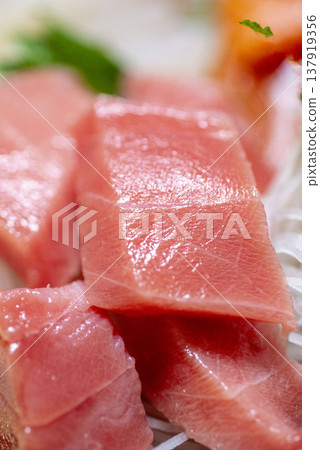 新鮮鮪魚刺身,切成小塊,配上白蘿蔔絲和紫蘇葉。特寫鏡頭展現了鮮亮的紅色魚肉。 新鮮鮪魚刺身,切成小塊,配上白蘿蔔絲和紫蘇葉。特寫鏡頭展現了鮮亮的紅色魚肉。 137919356