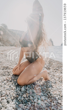 Woman beach pebbles kneeling on a shore under bright sun flares for a beautiful and relaxed tropical summer vacation Woman beach pebbles kneeling on a shore under bright sun flares for a beautiful and relaxed tropical summer vacation 137919659
