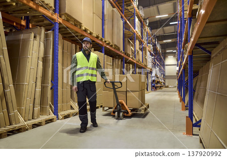 Warehouse worker operating pallet jack moving boxes on industrial storage shelves 137920992
