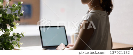 A woman working on her laptop with plants in the background. A woman working on her laptop with plants in the background. 137921182