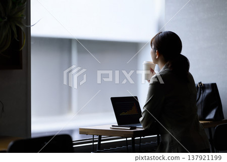 A woman working on her laptop while drinking coffee at a cafe. 137921199