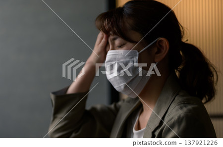 A woman wearing a mask is suffering from a headache. A woman wearing a mask is suffering from a headache. 137921226