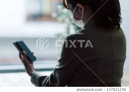 一名戴著口罩的女子正在操作智慧型手機。 137921256