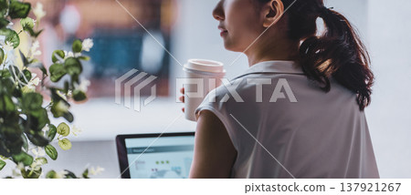 A woman is working on her PC with a drink in her hand. 137921267