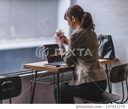 一位女士在咖啡館一邊喝咖啡一邊使用筆記型電腦工作。 137921274