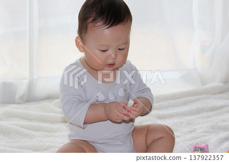 A 9-month-old baby sitting up and eating a snack. A 9-month-old baby sitting up and eating a snack. 137922357
