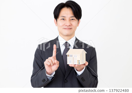 一位中年商人舉起一棟獨立式住宅的模型，並豎起食指。 137922480