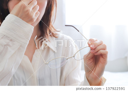 A woman with tired eyes; her hand holding her glasses. A woman with tired eyes; her hand holding her glasses. 137922591