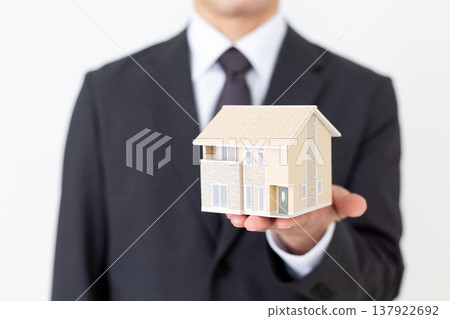 A middle-aged businessman with a model of a detached house. A middle-aged businessman with a model of a detached house. 137922692