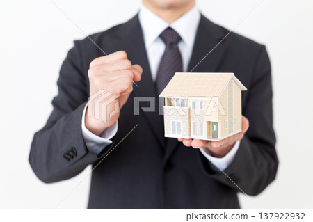 一位中年商人手持獨立式住宅模型,擺出勝利的姿態。 一位中年商人手持獨立式住宅模型,擺出勝利的姿態。 137922932