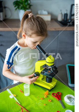 Close portrait of young girl looking through microscope during home science experiment. Focused scientific observation and early STEM education through hands on research activity. Close portrait of young girl looking through microscope during home science experiment. Focused scientific observation and early STEM education through hands on research activity. 137923104