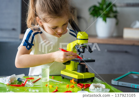 Young girl placing small grown crystal onto microscope slide during home science experiment. Detailed scientific observation and hands on STEM learning through crystal analysis. Young girl placing small grown crystal onto microscope slide during home science experiment. Detailed scientific observation and hands on STEM learning through crystal analysis. 137923105