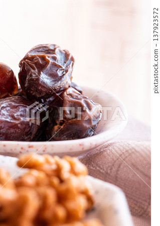 A close-up of two plates containing dates and walnuts, accompanied by cinnamon sticks prepared for Iftar at Ramadan. The scene highlights healthy snacks and natural ingredients. A close-up of two plates containing dates and walnuts, accompanied by cinnamon sticks prepared for Iftar at Ramadan. The scene highlights healthy snacks and natural ingredients. 137923572