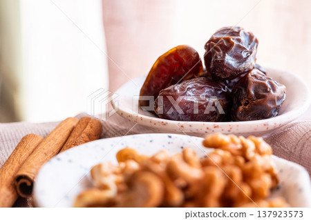 A close-up of two plates containing dates and walnuts, accompanied by cinnamon sticks prepared for Iftar at Ramadan. The scene highlights healthy snacks and natural ingredients. A close-up of two plates containing dates and walnuts, accompanied by cinnamon sticks prepared for Iftar at Ramadan. The scene highlights healthy snacks and natural ingredients. 137923573