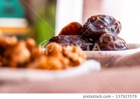 A close-up of two plates containing dates and walnuts, accompanied by cinnamon sticks prepared for Iftar at Ramadan. The scene highlights healthy snacks and natural ingredients. A close-up of two plates containing dates and walnuts, accompanied by cinnamon sticks prepared for Iftar at Ramadan. The scene highlights healthy snacks and natural ingredients. 137923579