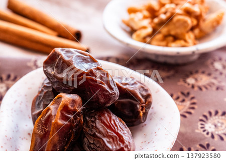 A close-up of two plates containing dates and walnuts, accompanied by cinnamon sticks prepared for Iftar at Ramadan. The scene highlights healthy snacks and natural ingredients. A close-up of two plates containing dates and walnuts, accompanied by cinnamon sticks prepared for Iftar at Ramadan. The scene highlights healthy snacks and natural ingredients. 137923580