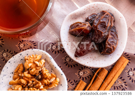 A close-up of two plates containing dates and walnuts, accompanied by cinnamon sticks prepared for Iftar at Ramadan. The scene highlights healthy snacks and natural ingredients. A close-up of two plates containing dates and walnuts, accompanied by cinnamon sticks prepared for Iftar at Ramadan. The scene highlights healthy snacks and natural ingredients. 137923586