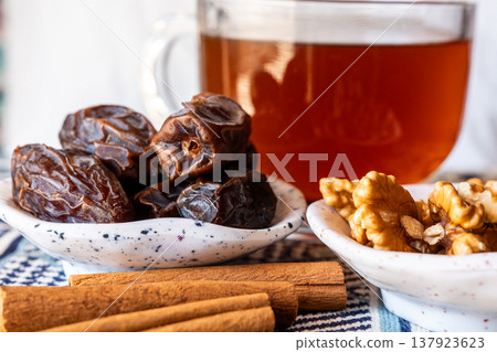 A close-up of two plates containing dates and walnuts, accompanied by cinnamon sticks prepared for Iftar at Ramadan. The scene highlights healthy snacks and natural ingredients. A close-up of two plates containing dates and walnuts, accompanied by cinnamon sticks prepared for Iftar at Ramadan. The scene highlights healthy snacks and natural ingredients. 137923623