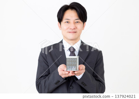 A middle-aged businessman holding a residential model of a corporate building. A middle-aged businessman holding a residential model of a corporate building. 137924021