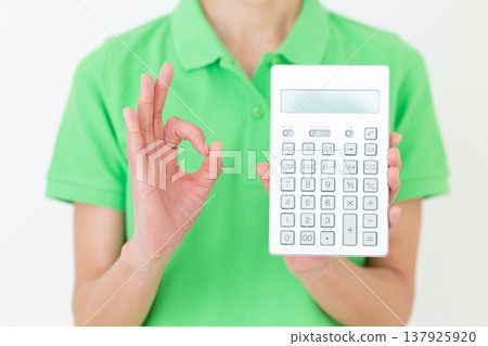 A middle-aged female care worker makes a circular gesture while holding a calculator. A middle-aged female care worker makes a circular gesture while holding a calculator. 137925920