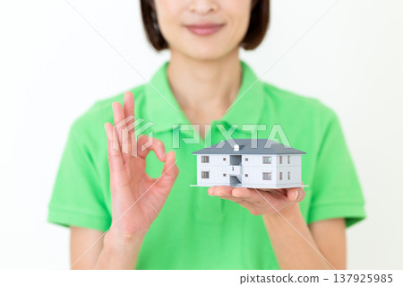 A middle-aged female care worker makes a circular pose while holding a model house. A middle-aged female care worker makes a circular pose while holding a model house. 137925985