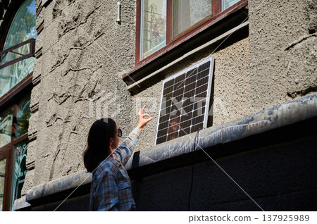 Woman holding photovoltaic solar panel in front of historical building, showing Ok sign. Concept of integration of sustainable renewable energy sources into old architecture. Woman holding photovoltaic solar panel in front of historical building, showing Ok sign. Concept of integration of sustainable renewable energy sources into old architecture. 137925989