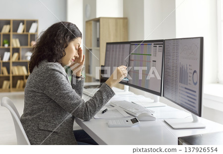 Tired female accountant massaging forehead at office computer during data analysis 137926554