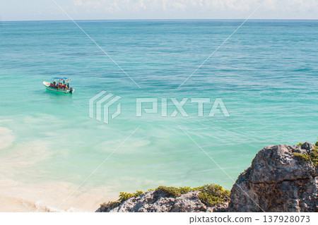 People vacationing on a small boat along the bright turquoise waters of the Caribbean Sea near Tulum, Mexico, enjoying a sunny day on a tropical beach holiday 137928073