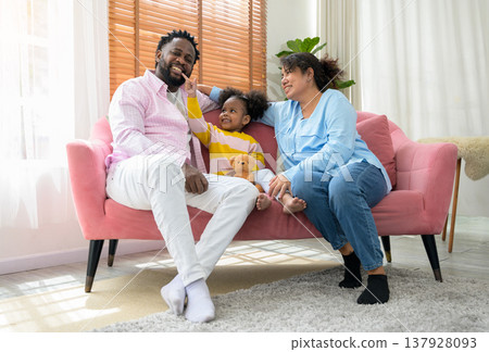 Joyful and playful multiethnic family of three sits together on pink sofa in living room at home Joyful and playful multiethnic family of three sits together on pink sofa in living room at home 137928093