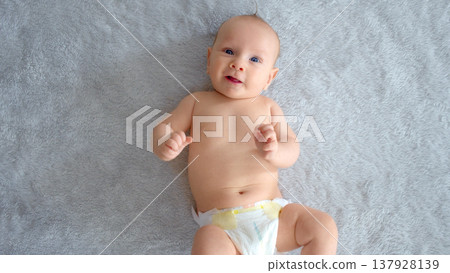 A healthy newborn baby in a nappy without clothes. Cute baby with blue eyes . Happy newborn boy lies on a blue blanket and actively moves his arms and legs. Half Full length body. 137928139