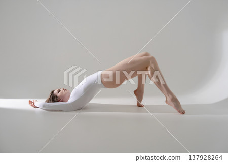 Flexible woman in white bodysuit doing bridge pose exercise on a minimalist gray background. Flexible woman in white bodysuit doing bridge pose exercise on a minimalist gray background. 137928264
