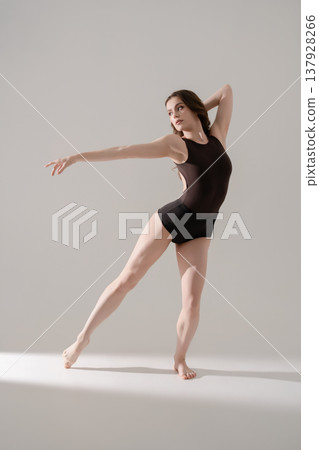 Elegant female dancer in a contemporary pose against a minimalist gray background. Elegant female dancer in a contemporary pose against a minimalist gray background. 137928266