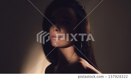 Low key portrait of woman with shadow across face in studio lighting. Low key portrait of woman with shadow across face in studio lighting. 137928322