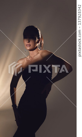 Elegant woman in black dress posing in studio with dramatic shadow lighting. Elegant woman in black dress posing in studio with dramatic shadow lighting. 137928342
